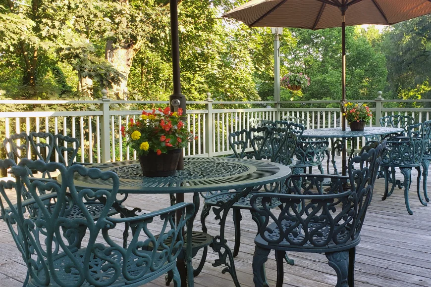 Wooden deck at Rocky Springs Bed and Breakfast, with wrought iron patio furniture, a market umbrella, and hanging flower baskets surrounded by trees