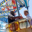 Father and son riding a hot air balloon-themed carnival attraction at Dutch Wonderland on Route 30 East, with a roller coaster visible in the background