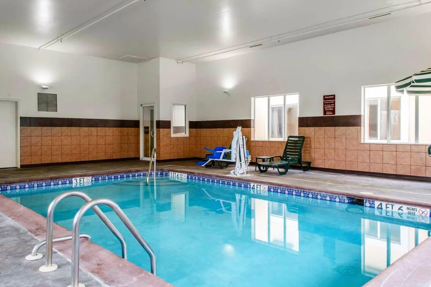 Indoor pool at Sleep Inn and Suites, with a pool lift, ladder rails, and lounge chairs beside tiled walls