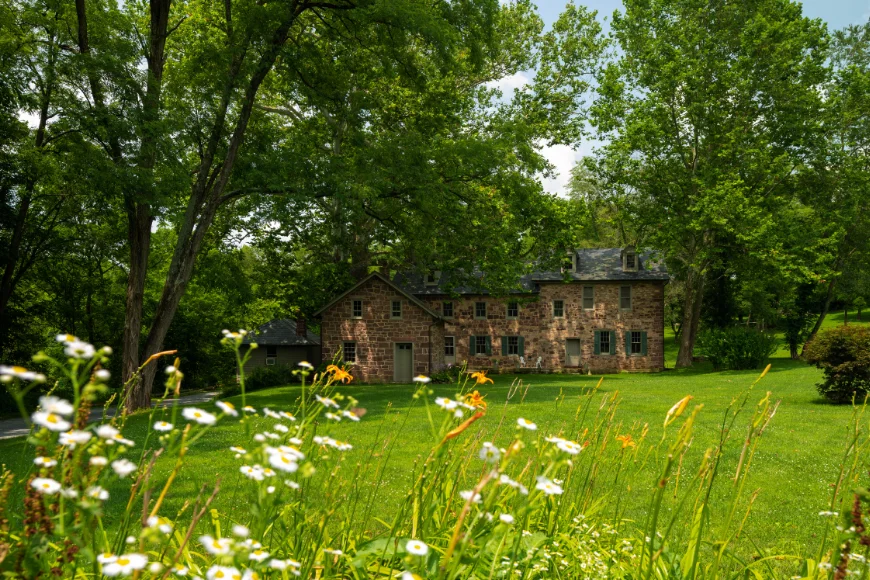 Speedwell Forge B&B image: stone forge building with wildflower meadow in the foreground, surrounded by mature trees in Lancaster, PA