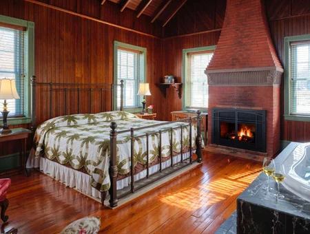 Speedwell Forge B&B suite image: bedroom with wood fireplace, iron bed frame, and wine glasses by a soaking tub in Lancaster, PA