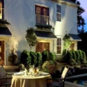 Poolside patio dining setup at Inn at Leola Village near suburban Lancaster, PA, with a set table, string lights, illuminated pool, and lush landscaping at dusk