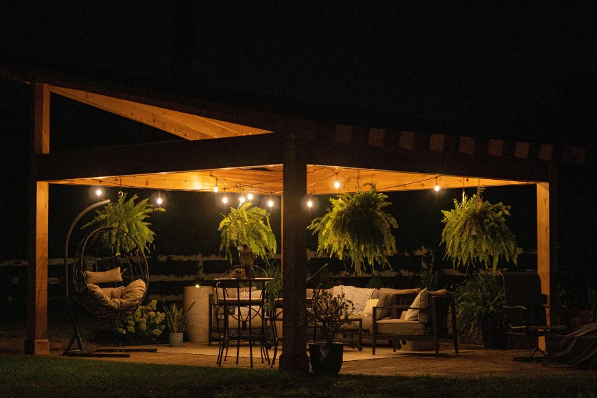 The Cottage and Loft outdoor pergola image: covered patio with string lights, hanging ferns, a hanging chair, and lounge seating at night in Lancaster, PA