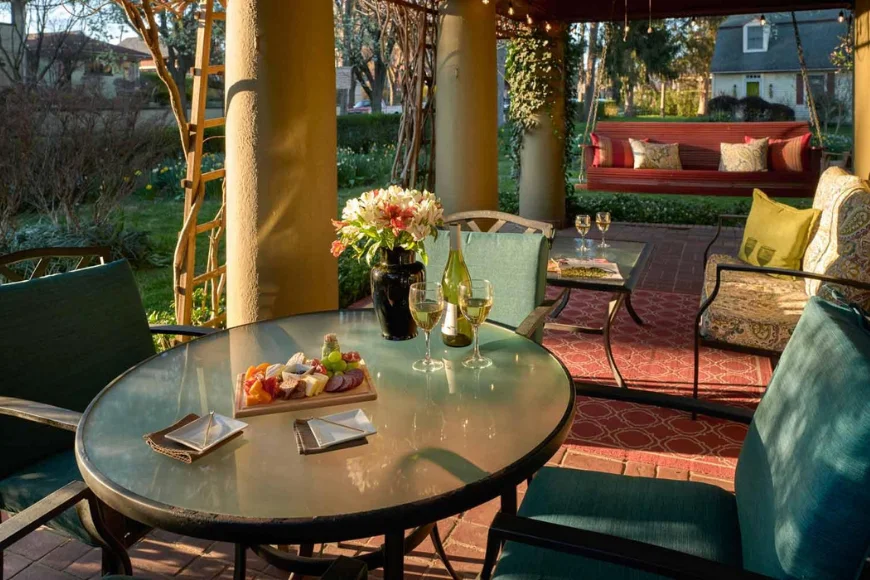 The Lancaster B&B deck image: covered porch with a bistro table set with wine and a charcuterie board, plus a red swing bench in Lancaster, PA