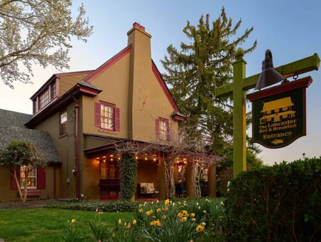 The Lancaster B&B exterior image: colonial home with red shutters, string lights on the covered porch, and an entrance sign in Lancaster, PA